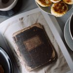A rustic breakfast arrangement with pastries, tea, and a vintage book in a cozy still life composition.